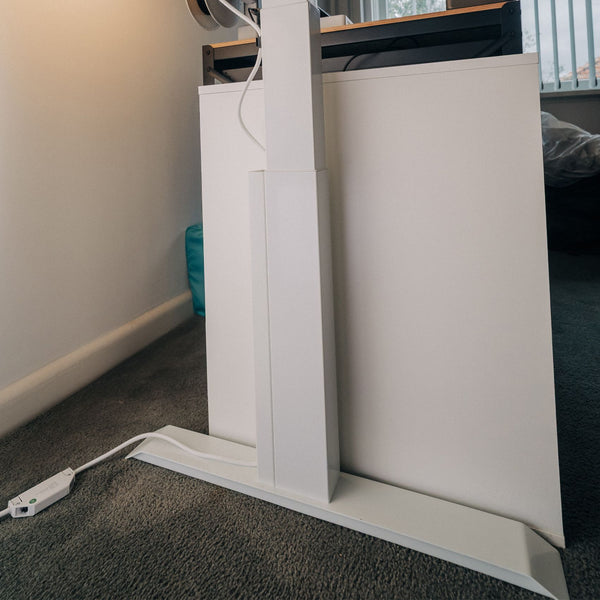 A close-up of a modern white standing desk with a magentic cable management attached