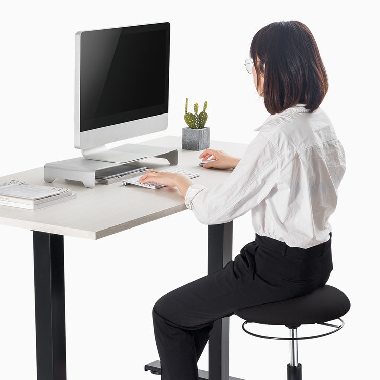 Woman sitting on active stool in front of standing desk